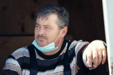 Medikal maske takan orta yaşlı beyaz bir adam düşünceli bir şekilde başka tarafa bakıyor.. 