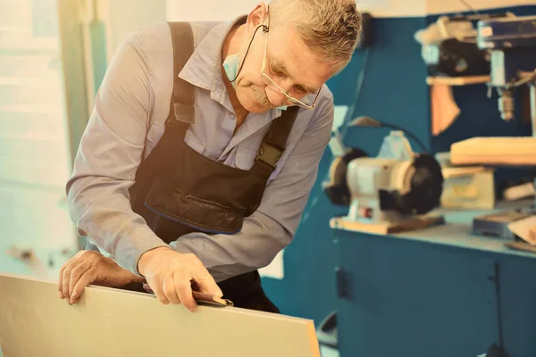 Portret van een bejaarde timmerman of timmerman werkend met houten planken in een timmermanswerkplaats. — Stockfoto