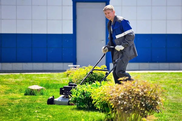 한 젊은 남자가 잔디깎는 기계를 타고 푸른 잔디 위를 걷고 있습니다.. — 스톡 사진