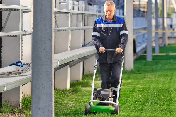 작업복에 종사하는 연금 생활자는 화창 한 날에 일하는 지역의 잔디깎는 기계와 함께 일한다. — 스톡 사진