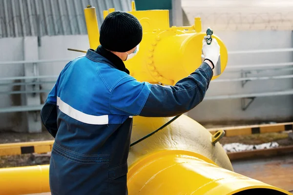 Çalışan elbiseli bir ressam, bir yaz günü kompresör tabancasından gaz çıkarmak için metal bir kapama vanası boyuyor.. 