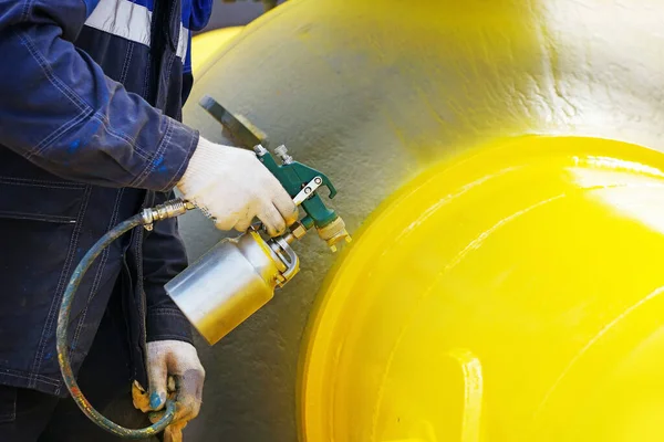 A painter in working clothes paints a metal shut-off valve for gasification from a compressor gun on a summer day. — Stock Photo, Image