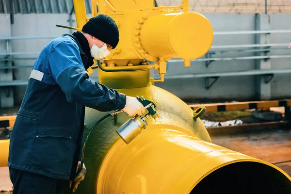 Çalışan elbiseli bir ressam, bir yaz günü kompresör tabancasından gaz çıkarmak için metal bir kapama vanası boyuyor.. 