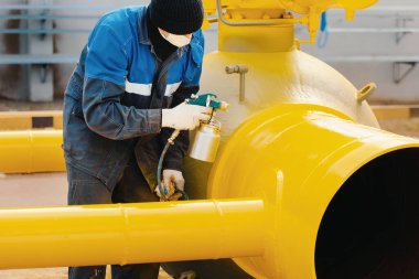 Çalışan elbiseli bir ressam, bir yaz günü kompresör tabancasından gaz çıkarmak için metal bir kapama vanası boyuyor.. 