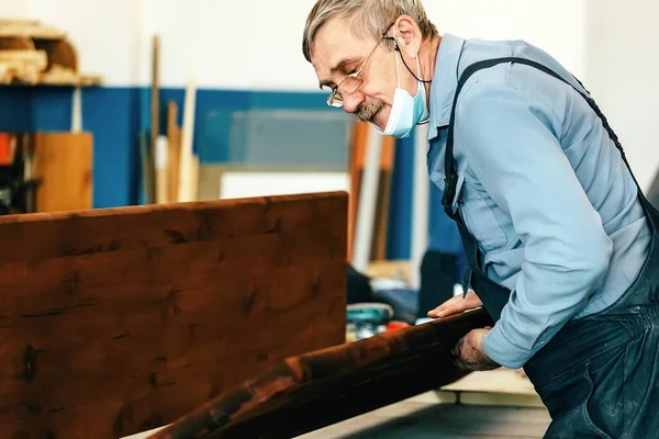 Gri saçlı, gözlüklü bir marangoz bir marangozhanedeki tezgahta ahşap ile çalışır.. — Stok fotoğraf