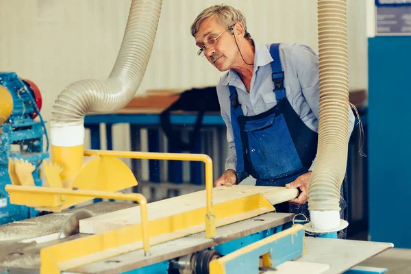 Un carpintero de edad avanzada trabaja en un taller de carpintería. Corte de tablas de madera. Escena auténtica. — Foto de Stock