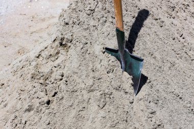 Gri kum yığınından bir kürek sarkıyor. Yapı malzemeleri. Yol veya onarım işi kavramı.