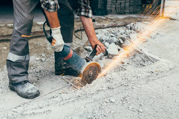Açı öğütücüsü olan bir işçi yolun beton kaldırımını keser ve kıvılcımlar uçuşur..