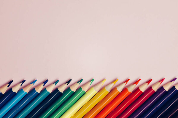 Colored pointed pencils lie on a pink background with space for copying. School supplies or school preparation.