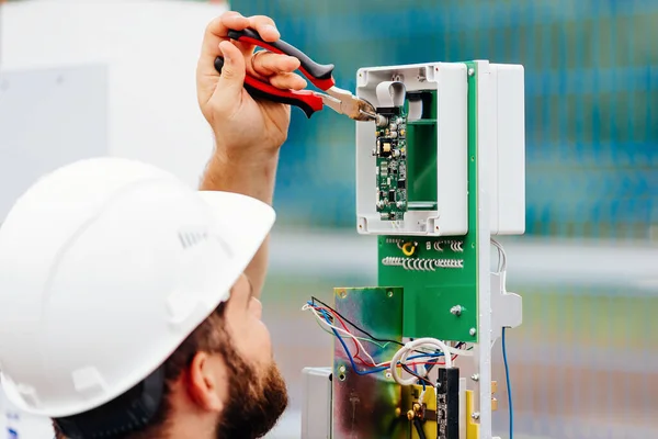 Un ingeniero eléctrico cualificado instala un dispositivo de control y medición en una instalación industrial en un día de verano. — Foto de Stock