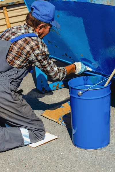 작업복을 입은 노인 이 페인트 붓으로 거리에 있는 쓰레기통이나 컨테이너를 물감으로 닦고 있다. — 스톡 사진