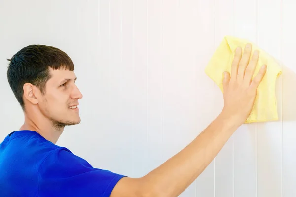 A young Caucasian guy washes the wall with a rag and smiles. A cheerful clearing service worker. Washing of premises.