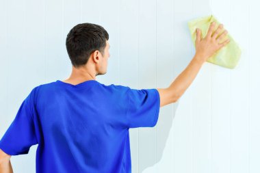 Elinde bez parçası olan bir adam odanın içindeki duvarı yıkıyor..