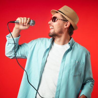 Şapkalı orta yaşlı bir adamın portresi elinde bir mikrofon tutuyor ve duygusal olarak bir şarkı söylüyor..