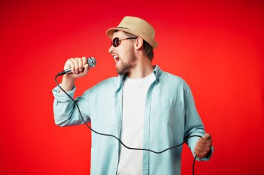 Şapkalı orta yaşlı bir adamın portresi elinde bir mikrofon tutuyor ve duygusal olarak bir şarkı söylüyor..