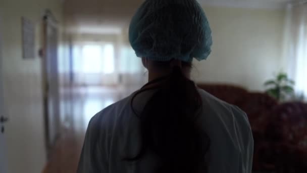 Zmęczona kobieta lekarz w ubraniu medycznym powoli idzie pustym korytarzem kliniki medycznej lub szpitala. — Wideo stockowe