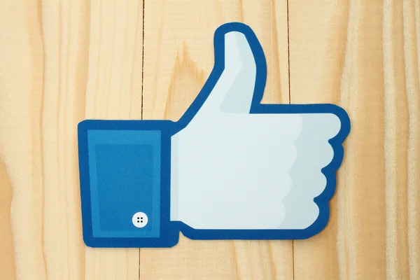 Facebook thumbs up sign printed on paper and placed on wooden background. — Stock Photo, Image