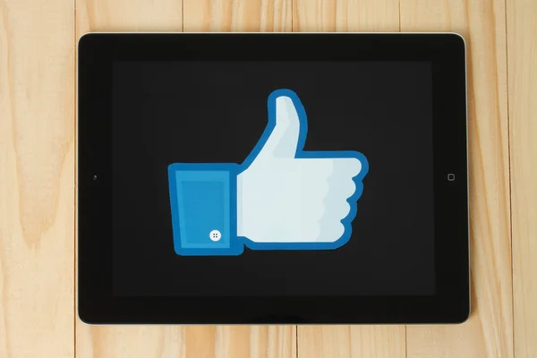 Facebook thumbs up sign printed on paper and placed on iPad on wooden background — Stock Photo, Image