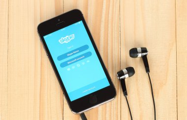 iPhone with Skype logotype on its screen and headphones on wooden background