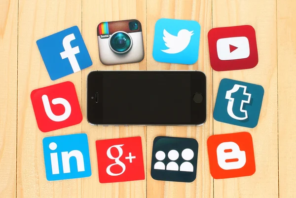 Ícones de mídia social famosos colocados em torno do iPhone em fundo de madeira — Fotografia de Stock