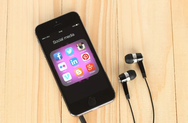 Smart phone with social media logos on its screen and headphones on wooden background — Stock Photo, Image