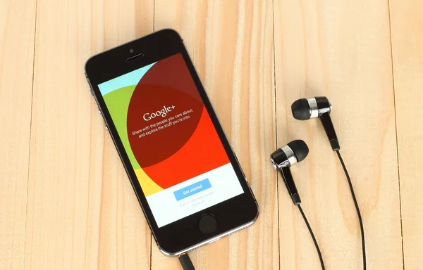 IPhone with Google Plus logotype on its screen and headphones on wooden background — Φωτογραφία Αρχείου