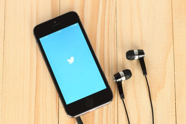 :iPhone с логотипом Twitter на экране и наушниками на деревянном фоне — стоковое фото