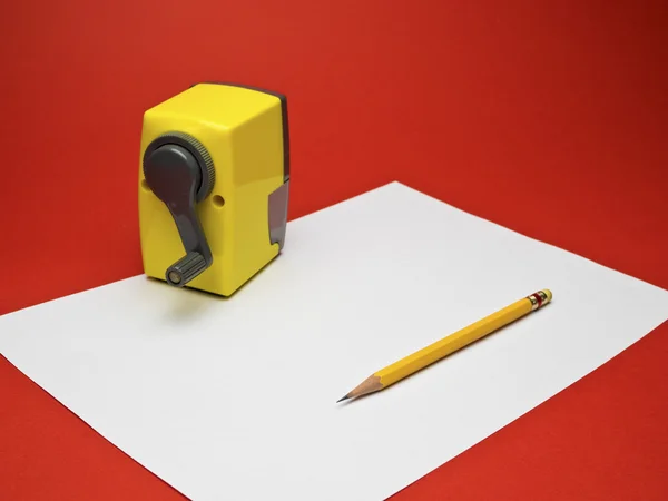 Lápis amarelo e apontador sobre papel branco com fundo vermelho — Fotografia de Stock