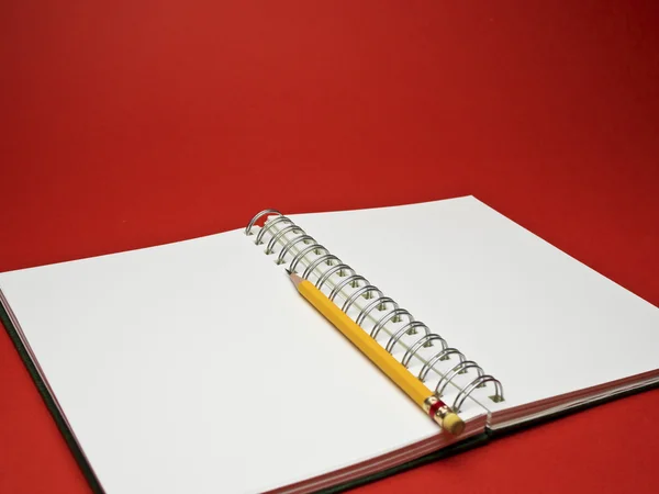 Lápis amarelo no caderno branco com fundo vermelho — Fotografia de Stock