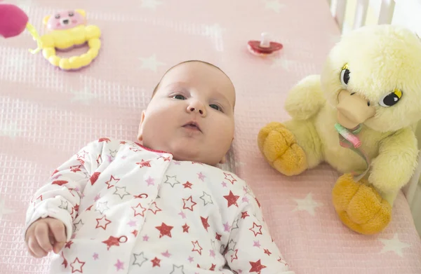 Meisje van de baby in een bed met speelgoed — Stockfoto