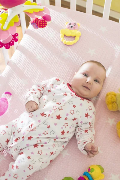 Meisje van de baby in een bed met speelgoed rond — Stockfoto