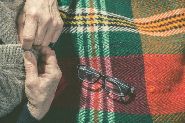 老年妇女扣着他的背心 毯子上的眼镜 — 图库照片