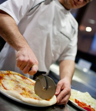Mutfakta pizza kesen beyaz üniformalı aşçının yakın çekimi.