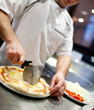 Mutfakta pizza kesen beyaz üniformalı aşçının yakın çekimi.