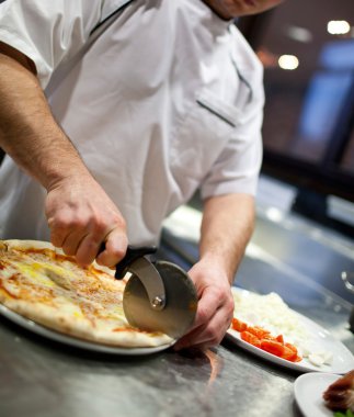 Mutfakta pizza kesen beyaz üniformalı aşçının yakın çekimi.