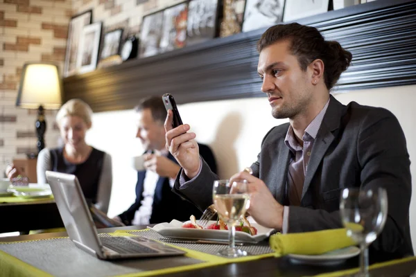 Młody mężczyzna pracujący z laptopa używa telefonu. Jego koledzy prowadzenia rozmowy — Zdjęcie stockowe
