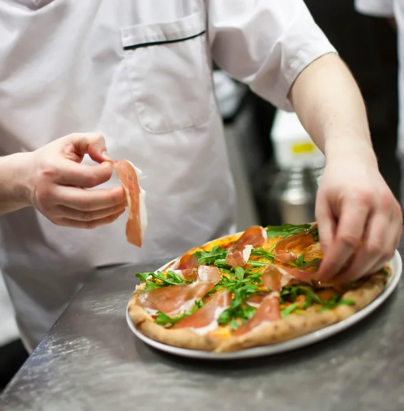 Şef mutfakta pizza yapıyor.