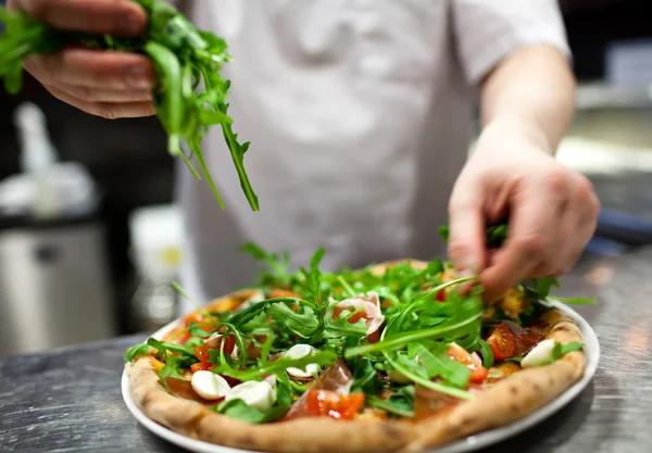 Şef mutfakta pizza yapıyor.