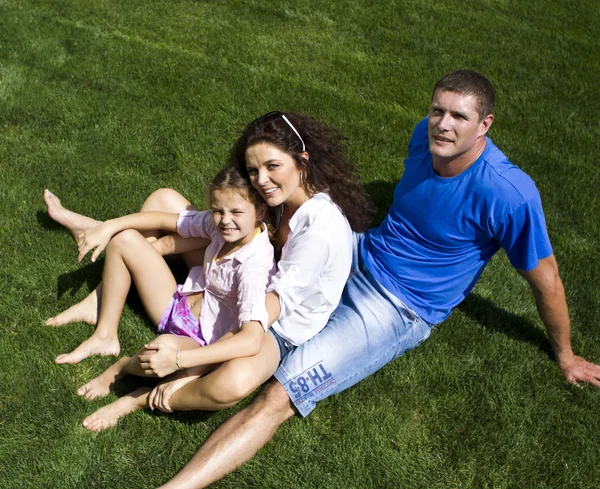 Feliz bela jovem família deitada na grama verde. Três pessoas alegres — Fotografia de Stock