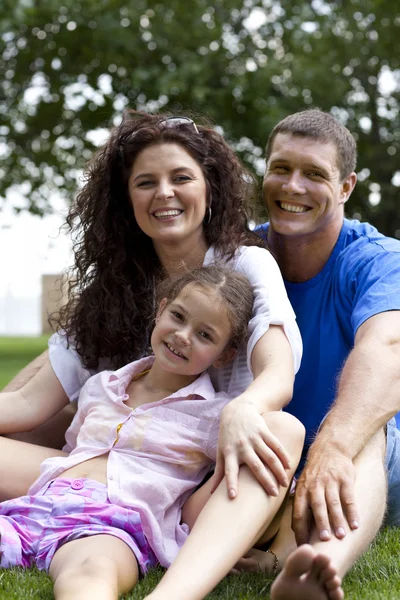 Glücklich schöne junge Familie auf dem grünen Gras liegend. drei fröhliche Menschen — Stockfoto