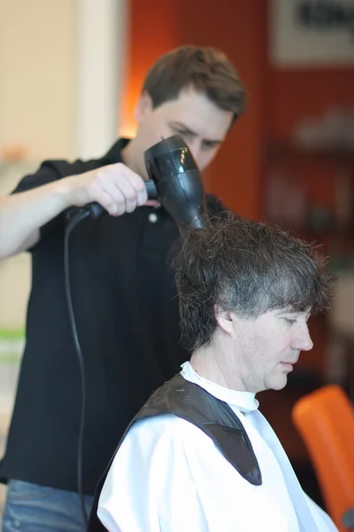 Un hombre corta el pelo en una barbería. Maestro joven estilista. Céntrate en el pelo gris —  Fotos de Stock