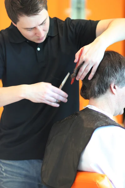 Un hombre corta el pelo en una barbería. Maestro joven estilista. Céntrate en el pelo gris — Foto de Stock
