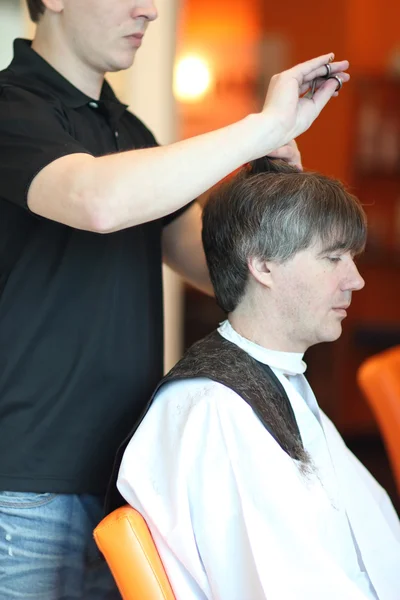 Un hombre corta el pelo en una barbería. Maestro joven estilista. Céntrate en el pelo gris —  Fotos de Stock