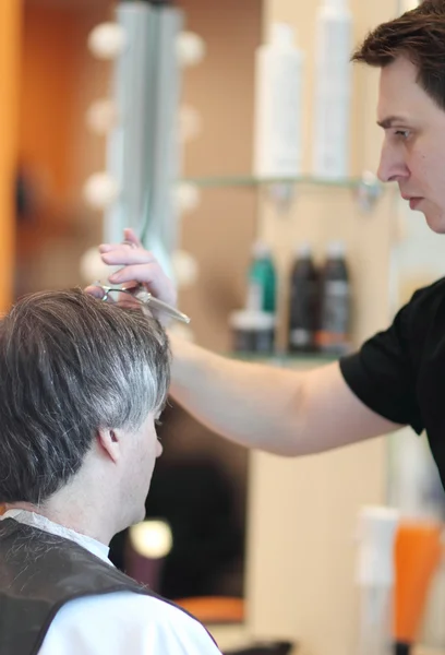 男は理髪店で髪をカットします。マスター若いスタイリスト。グレーの髪に焦点を当てる — ストック写真