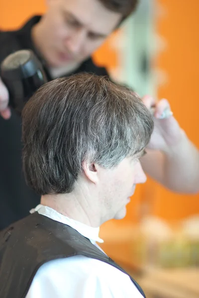 Um homem corta cabelo numa barbearia. Mestre jovem estilista. Concentre-se em cabelos grisalhos Imagem De Stock