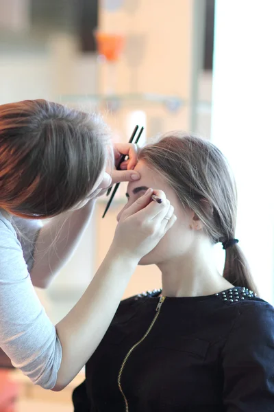 Joven maestro de maquillaje mirando el maquillaje de la mujer en el salón — Foto de Stock