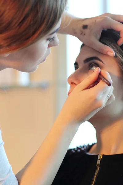 Joven maestro de maquillaje mirando el maquillaje de la mujer en el salón — Foto de Stock