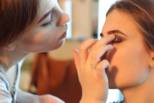 Joven maestro de maquillaje mirando el maquillaje de la mujer en el salón — Foto de Stock