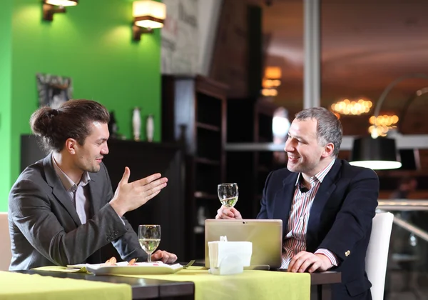 Два улыбающихся бизнесмена едят в ресторане — стоковое фото