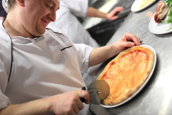 Närbild hand kock bagare i vit uniform skära pizza i köket — Stockfoto